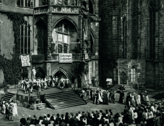 Historische Szene einer Aufführung und vielen Zuschauern.