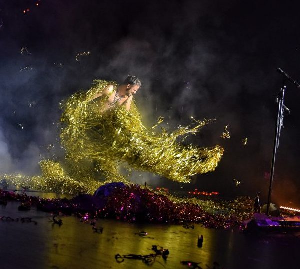 Leuchtende Figur aus Farben und Licht auf reflektierendem Bühnenboden.